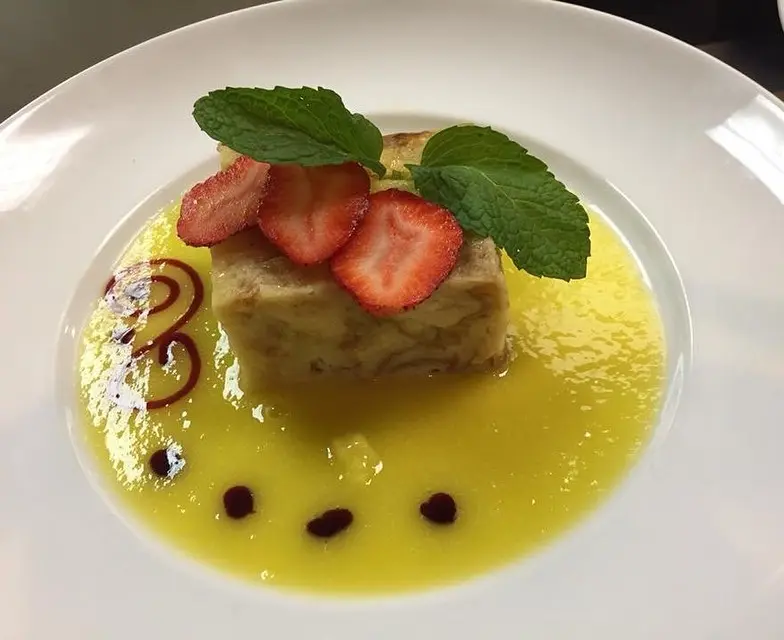 Bread pudding in white chocolate sauce topped with strawberries and mint