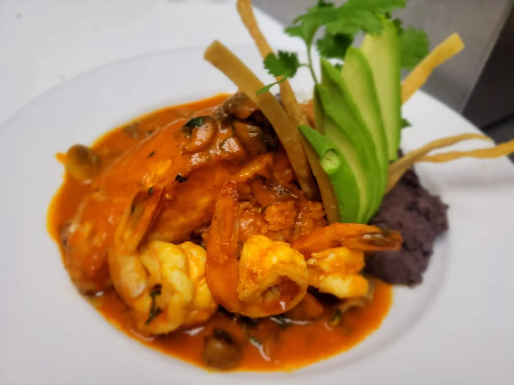 Shrimp in red guajillo chile sauce with sliced avocado and black beans