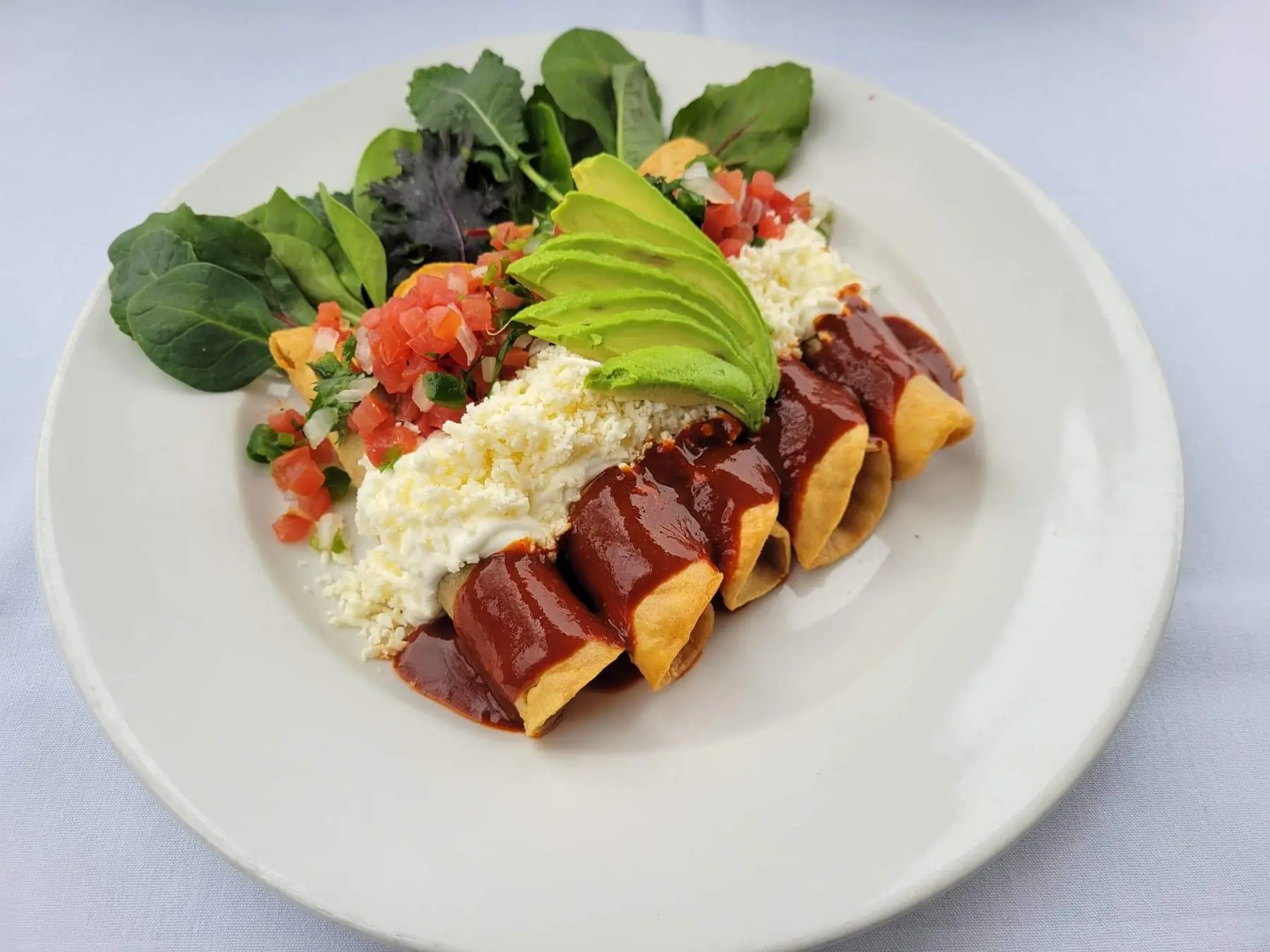 Enchiladas in red sauce topped with queso fresco, pico de gallo and avocado