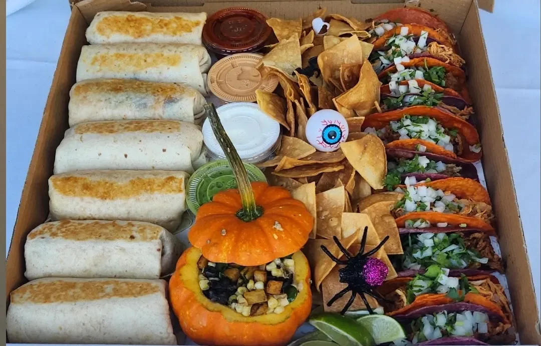 Mini burritos and tacos around a pumpkin filled with queso and corn, with plastic spiders and candy eyes
